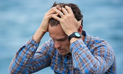A man in a blue plaid shirt holding his head in his hands, illustrating overwhelming anxiety and the need for coping skills.